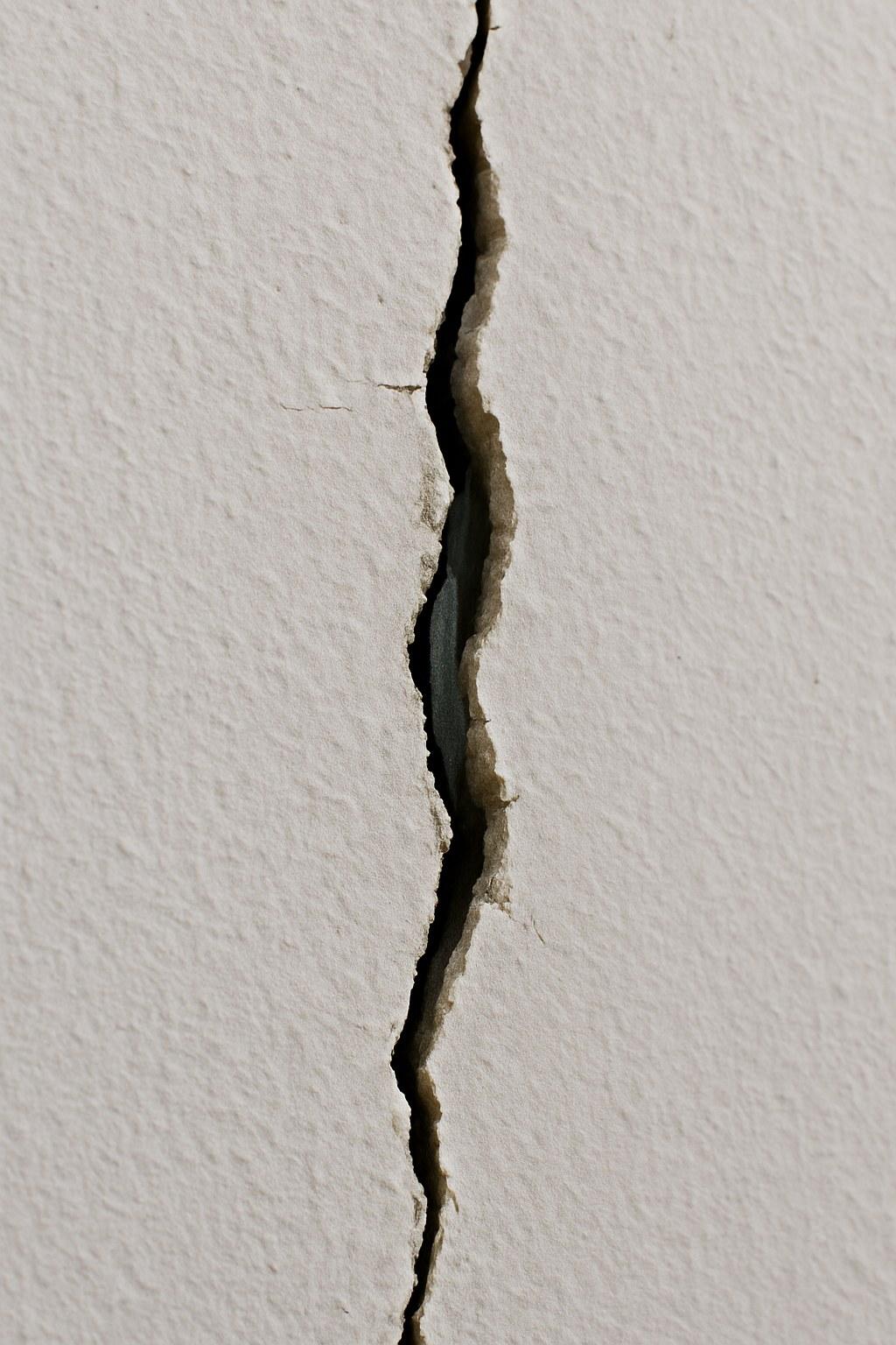 A hairline crack in a white wall exposing a piece of metal.