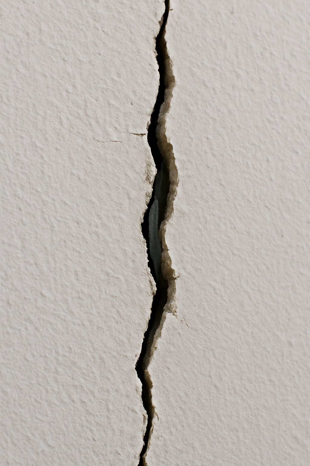 A hairline crack in a white wall exposing a piece of metal.